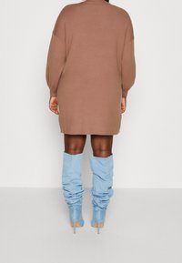 Braunes, gestricktes, oversized Kleid mit langen Ärmeln, kombiniert mit hellblauen, lässigen kniehohen Stiefeln mit Absatz.