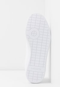 Sola di sneaker bianca su uno sfondo bianco, caratterizzata da un motivo di presa testurizzato e il marchio Lacoste.