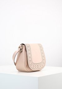 Rosa läder crossbody-väska med en perforerad lock, guldfärgad hårdvara, triangulär form och justerbar rem. Slät textur med accenter.