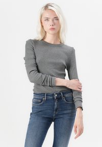 Gray long-sleeve t-shirt with a round neck and ribbed texture, paired with fitted dark blue jeans featuring standard pockets and gold accents.