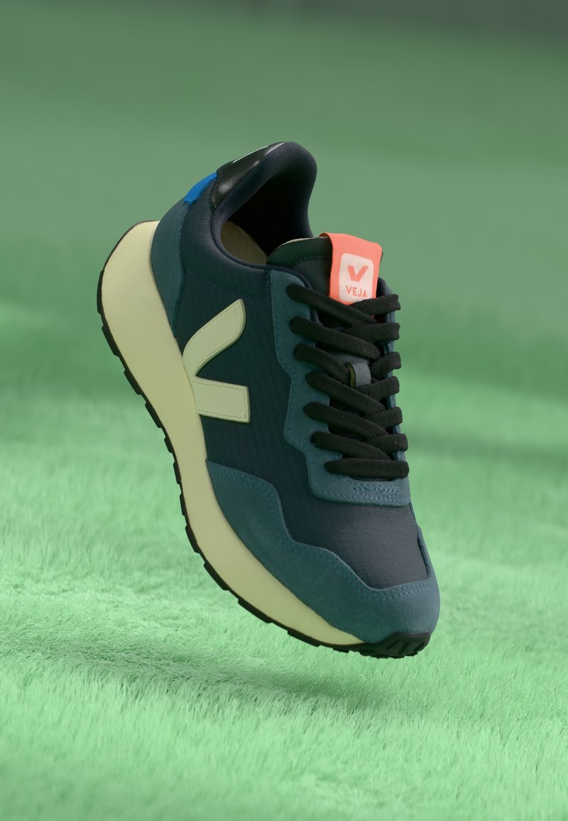 Navy and teal sneaker with a textured surface, black laces, soft cream sole, and a pink accents on the heel tab and branding.