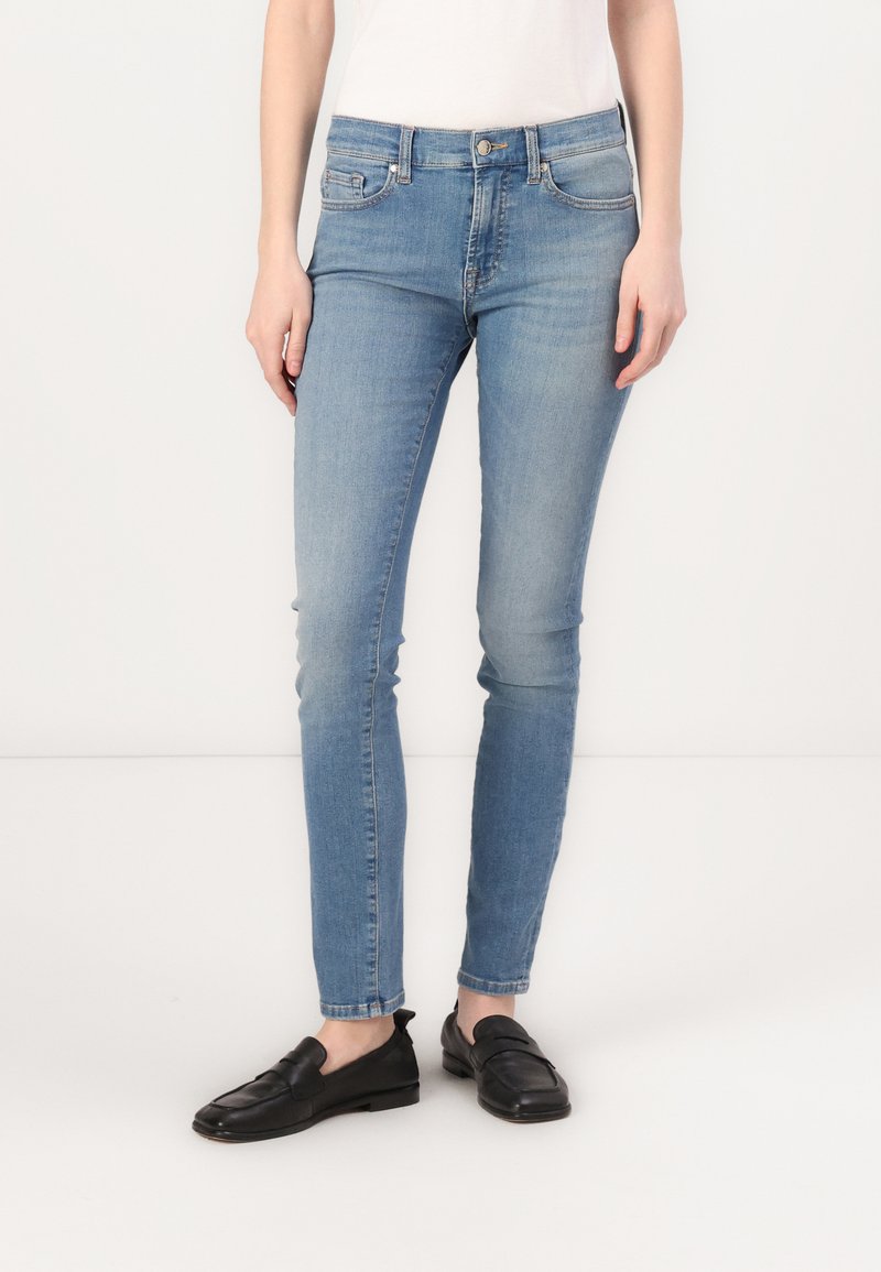 Svijetloplave skinny traperice od rastezljive tkanine s dizajnom s pet džepova, srednjim strukom i izblijedjelim završetkom. Nosene uz crne natikače.