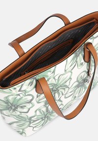 Kukkakuviollinen kangaskassi valkoisella pohjalla, ruskeilla nahkakahvoilla ja mustalla vetoketjullisella sisäosalla, jossa on hienovarainen raidallinen kuvio.