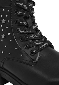 Stivale alla caviglia nero in pelle sintetica con borchie e stelle decorative argentate. Presenta lacci neri con il marchio "Pepe Jeans".