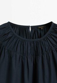 Abbigliamento blu navy con texture arricciata intorno al collo, dotato di chiusura a bottone sul retro e realizzato in un tessuto morbido e leggero.