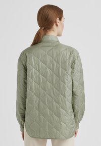 Gepatchte Jacke in Hellgrün mit einem strukturierten, wellenförmigen Muster. Verfügt über einen klassischen Kragen und lange Ärmel, gestaltet mit einem abgerundeten Saum.