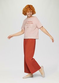 Lichtroze T-shirt met korte mouwen met bedrukt tekst, gecombineerd met brede roestkleurige broek en beige geweven instappers.