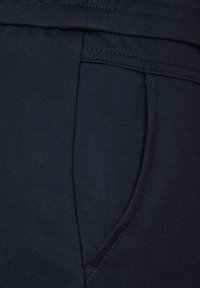 Nahaufnahme von marineblauem Stoff, der eine Tasche mit einer sauberen Naht zeigt. Das Material wirkt glatt mit einem leichten Glanz, was seine strukturierte Textur betont.