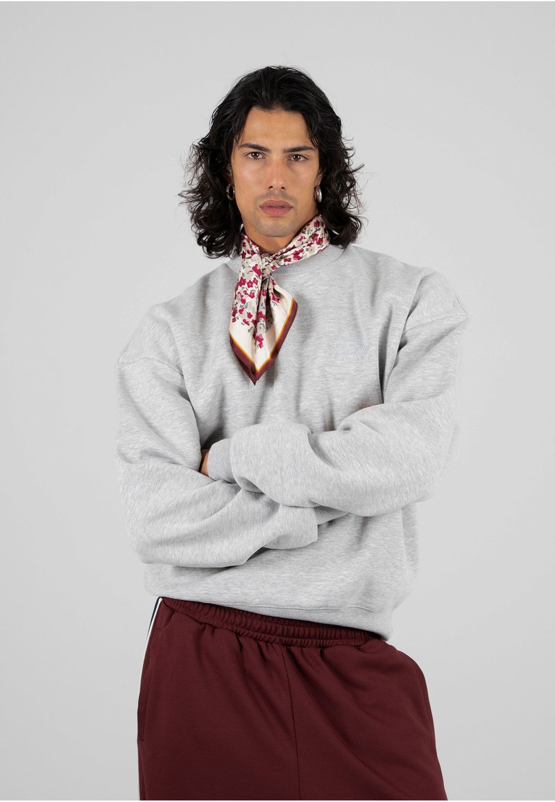 Felpa grigia con spalle cadute, texture in fleece; abbinata a pantaloni corti bordeaux. Notevole sciarpa di seta con stampa floreale attorno al collo.