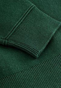 Dunkelgrüner Strickpullover mit gerippten Bündchen und Saum. Die Textur wirkt weich mit einer glatten Oberfläche und zeigt gleichmäßige Nähte.