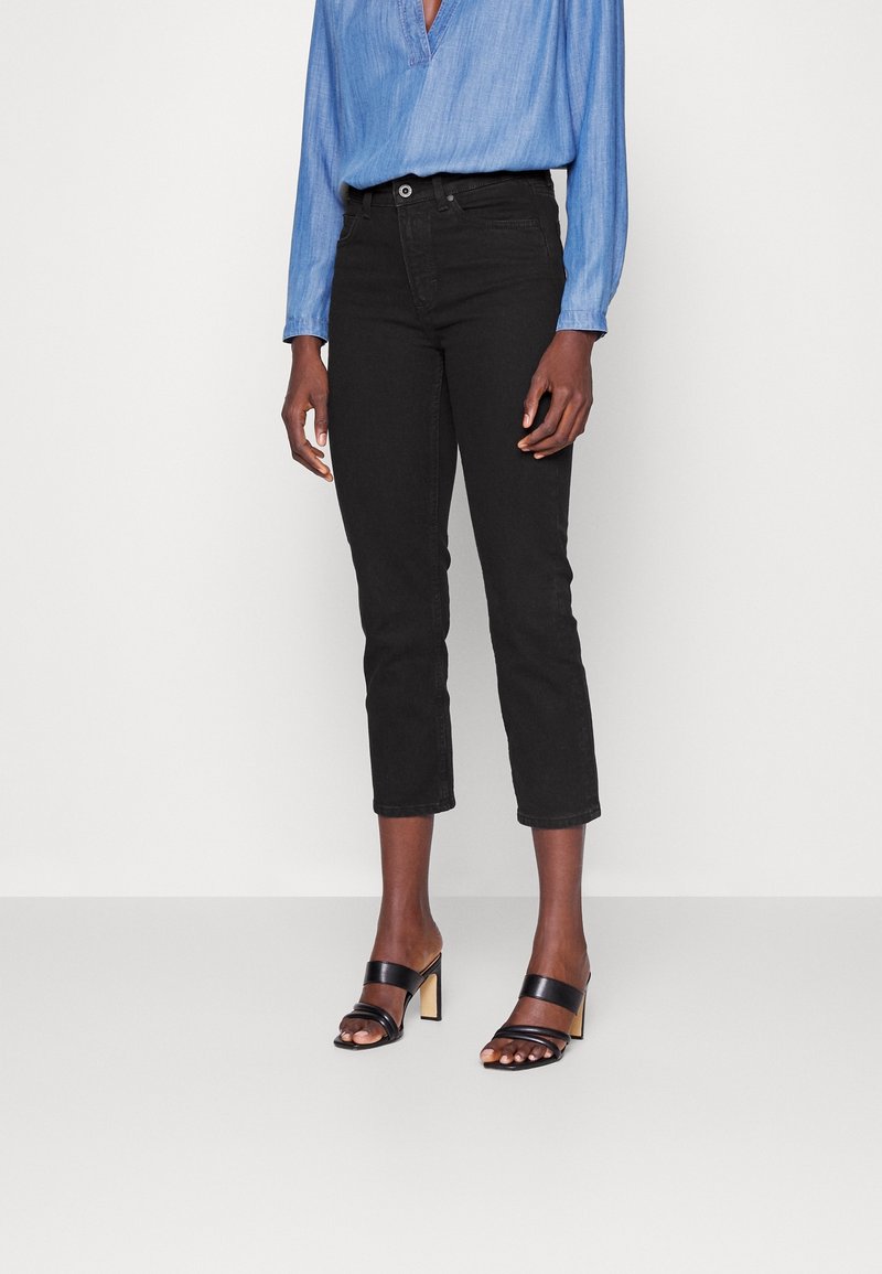 Jeans cropped negros en un diseño ajustado con cierre de botón, acompañados de sandalias negras de tacón con estilo de dos tiras y tacón cuadrado.