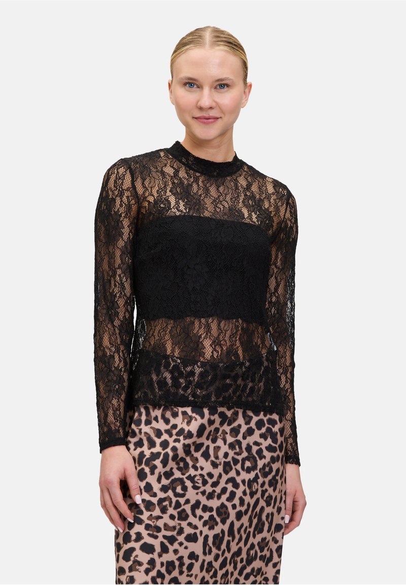 Schwarzes Spitzentop mit langen Ärmeln und hohem Kragen, das ein durchsichtiges Design aufweist. Kombiniert mit einem Leopardenmuster-Rock.