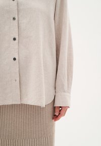 Cream linen button-up shirt with a relaxed fit, long sleeves, and subtle texture, paired with a ribbed beige skirt.