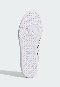 Suela de zapatilla de goma blanca con patrones texturizados para mayor agarre, con un logo en relieve circular y un diseño aerodinámico.