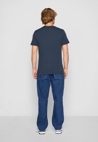 Navy blue short-sleeve t-shirt with a round neckline, paired with loose-fitting blue denim jeans and white sneakers.
