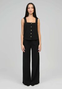 Top sans manches noir avec décolleté carré et cinq boutons dorés ; associé à un pantalon large noir. Tissu lisse, design minimaliste.