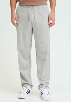 Graue Jogginghose aus weichem Stoff mit elastischem Bund und Kordelzug. Verfügt über Seitentaschen und eine lockere Passform, kombiniert mit weißen Turnschuhen.