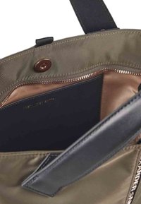 Interno di una borsa di tessuto verde oliva con una cerniera in bronzo, fodera nera e dettagli in pelle. Presenta una chiusura con bottone a pressione.