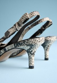 Schwarz-weiße Schlangenprint-Pumps mit Knöchelriemen und schlankem Absatz. Strukturierte Außenseite mit glattem Innenfutter.