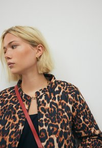 Jaguarprint jakke med stående krave, sorte og orange mønstre samt en let tekstur. Accenteret med en rød rem.