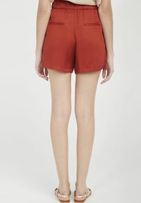 Rostfärgade shorts med resårmidja, två bakfickor och en slät yta. Sömmen är rak och slutar ovanför mitten av låret.