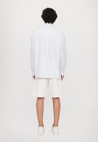 Camicia a righe azzurre chiaro con maniche lunghe, abbinata a pantaloni corti di lino bianchi. Sneakers bianche completano l'outfit.