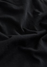 Tissu noir avec une texture fine en tricot, présentant des plis doux et des rides légères créant des ombres subtiles.