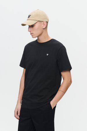 Svart bomullströja med kort ärm, rund halsringning och en liten logotyp på bröstet. Kombinerad med en beige keps med svart text.