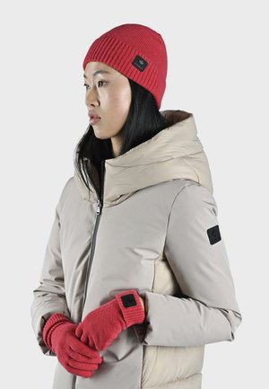Lichtbeige pufferjack met hoge kraag, rode ribgebreide beanie en handschoenen, voorzien van logo patches. Gladde textuur, slim fit.