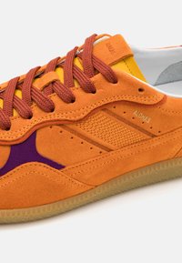 Orangenes Wildleder-Sneaker mit braunen Schnürsenkeln und gelben Akzenten. Verfügt über lila Details und ein strukturiertes Seitenpaneel. Gummisohle mit dreieckigem Profil.