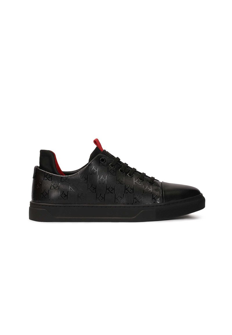 Zapatillas negras con patrón de logo en relieve, parte superior de piel lisa, punta redonda, acentos rojos contrastantes y suela de goma plana.
