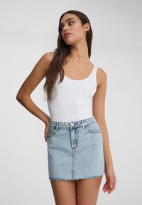 Canottiera bianca con piccole borchie argentate, abbinata a una mini gonna in denim blu chiaro con orlo sfrangiato e accenti metallici.