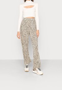 Weißes geripptes Crop-Top mit Ausschnitt und langen Ärmeln, kombiniert mit beigen Hose im Leopardenmuster mit lockerer Passform und ausgestellten Beinen.