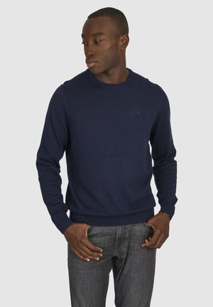 Navy blue crew neck sweater with long sleeves, made of a soft fabric, featuring ribbed cuffs and hem, and a subtle logo detail on the chest.