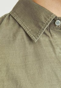 Cămașă din corduroy verde măsliniu cu un guler structurat, textură cu dungi verticale și un singur nasture la închidere.