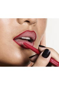 Rode lippenpotlood wordt op de lippen aangebracht; matte lichtroze lippen met een gedefinieerde rode rand; gladde huid; zwarte nagellak op de vingers.
