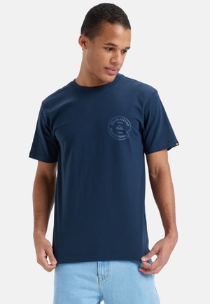 Camiseta de algodón azul marino con estampado de logotipo circular en el pecho, mangas cortas y cuello redondo. Textura suave.