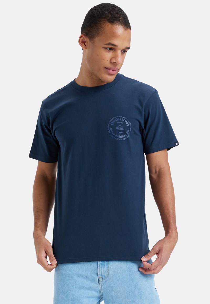 Camiseta de algodón azul marino con estampado de logotipo circular en el pecho, mangas cortas y cuello redondo. Textura suave.