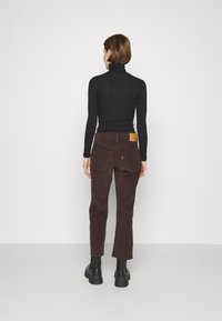 Pantalones de pana marrones con corte recto, que cuentan con un parche de marca de cuero en la parte trasera y bolsillos laterales profundos. Llevados con una blusa negra.