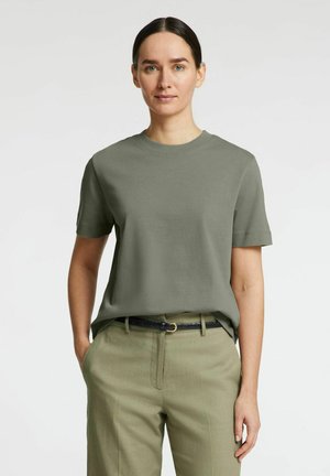 Olivengrøn kortærmet t-shirt i blødt stof, med rund hals og afslappet pasform, parret med lysegrønne bukser og et sort bælte.