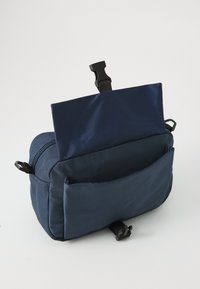 Marinefarbene Stofftasche mit einem Reißverschluss-Hauptfach, einer Vordertasche und einem verstellbaren Riemen. Enthält einen Kunststoffclip zur Sicherung des oberen Klappens.