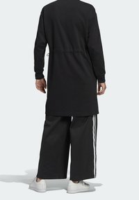 Černá tunika s dlouhým rukávem a staženým pasem, doplněná černými kalhotami s širokými nohavicemi a bílými pruhy. Hladká látka s volným střihem.