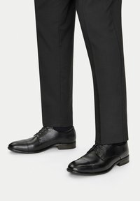 Mustad nahast kingad sileda pinnaga, nööbiga disainiga ja ümarate varvastega, mis on kombineeritud tumedate kohandatud pükstega.