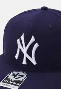 Gorra snapback azul marino con un logotipo de NYC bordado en blanco, que presenta una tela texturizada y una etiqueta de marca en el panel frontal izquierdo.