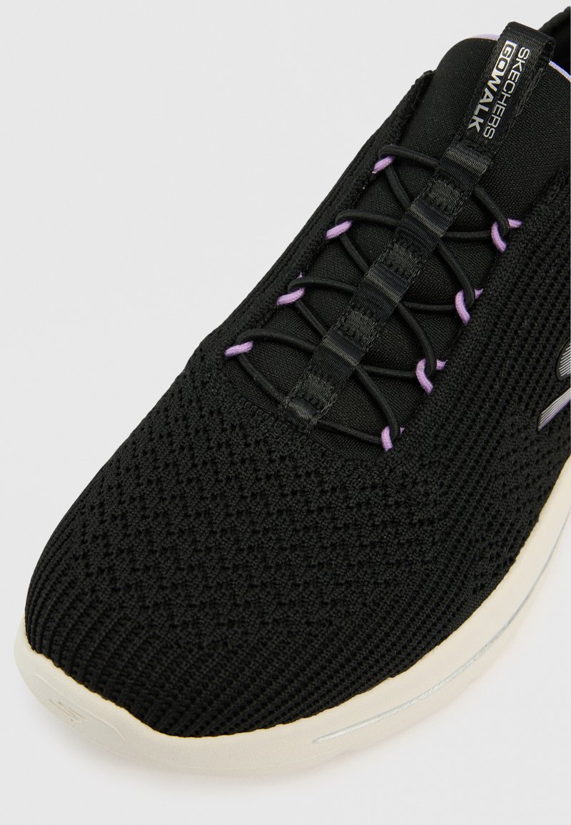 Zwarte Skechers Go Walk-schoen met een getextureerde gebreide bovenkant, voorzien van paarse veters, een ronde neus en een witte zool met een reflecterende accenten.