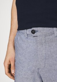 Pantalon en lin gris clair avec une finition texturée, doté d'un bouton de fermeture, de passants de ceinture et d'une coupe droite.