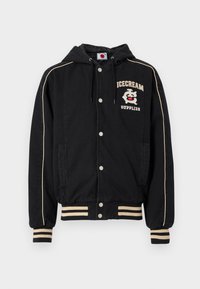 Μαύρο μπουφάν με κουκούλα, λευκές λεπτομέρειες, κουμπιά με πατιλέτα και δύο τσέπες στο πλάι. Φέρει το γράφημα «ICECREAM SUPPLIES» στο στήθος. Υλικό από βαμβακερό μείγμα.