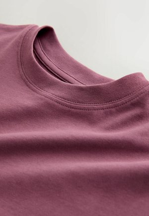 Fialové bavlněné tričko s kulatým výstřihem, měkkou texturou a pečlivě prošitými švy. Látka působí hladce, bez vzorů či grafiky.