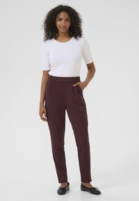 Pantaloni bordeaux a vita alta con pieghe frontali e tasche laterali; abbinati a un top fitted bianco a maniche corte e ballerine nere.