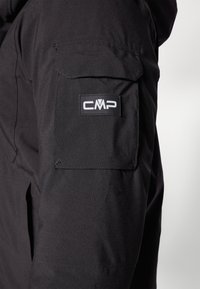 Schwarze isolierte Jacke mit einer Textur, die eine linke Arm-Tasche, das markierte CMP-Logo und ein langlebiges Gewebe-Design für Outdoor-Bekleidung aufweist.